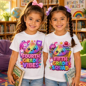 May include: Two white short-sleeve t-shirts featuring colorful graphic prints. One shirt displays a rainbow dumpling with school supplies and the text 'FOURTH GRADE VIBES'. The other shirt shows a similar design with the text 'FIFTH GRADE SQUAD'.