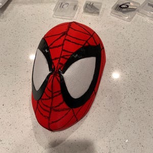 Op de afbeelding: Een rood Spider-Man-masker met zwarte webdetails en grote witte mesh oogopeningen. Dit masker bedekt het hele hoofd en is waarschijnlijk bedoeld voor cosplay of kostuums. Het ontwerp is een klassieke weergave van de iconische look van de superheld.
