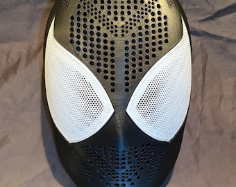 Könnte beinhalten: Eine schwarze Vollmaske mit einer texturierten Oberfläche, die zahlreiche kleine kreisförmige Perforationen im Stirn- und Kinnbereich aufweist. Die Maske verfügt über zwei große, weiße, netzbespannte Augenöffnungen in kantiger Form.