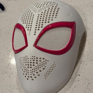 Könnte beinhalten: Eine weiße Vollgesichtsmaske mit perforierter Textur im Stirn- und Kinnbereich. Die Maske verfügt über zwei große, mandelförmige Augenöffnungen mit einem leuchtend pinken Rand und einem feinen weißen Netzgewebe über den Augenpartien.