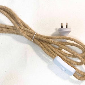May include: A coiled beige fabric-covered electrical cable featuring a white two-pin plug and a white inline rocker switch. The cable ends are stripped, revealing blue and brown internal wires, and the entire length is secured with a small white tie.
