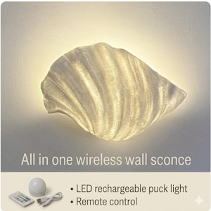 May include: A seashell-shaped wall sconce emitting a warm glow. Text reads: All in one wireless wall sconce. Below, an LED rechargeable puck light, a remote control, and a USB charging cable are displayed with the text: LED rechargeable puck light, Remote control.