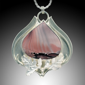 May include: A silver pendant featuring a teardrop-shaped stone with pink, white, and grey banded patterns and a dark black inclusion at the base. The stone is encased in a polished silver frame adorned with detailed silver leaf accents.