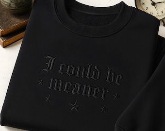 Könnte beinhalten: Schwarzes Sweatshirt mit dem gestickten Schriftzug "I could be meaner" in gotischer Schrift, ergänzt durch Sterne. Das Rundhals-Sweatshirt ist einfarbig schwarz.