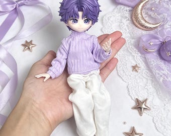 May include: A doll with purple hair, wearing a light purple sweater and white trousers. The doll is held in a hand, with decorative stars, ribbons, and a crescent moon in the background. The doll's eyes are a light purple.