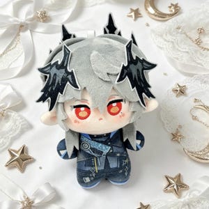 May include: A plush doll with gray hair and black accents, red eyes, and a blue outfit. The doll has a detailed design, with a crown-like feature on its head. The background includes decorative stars and ribbons.