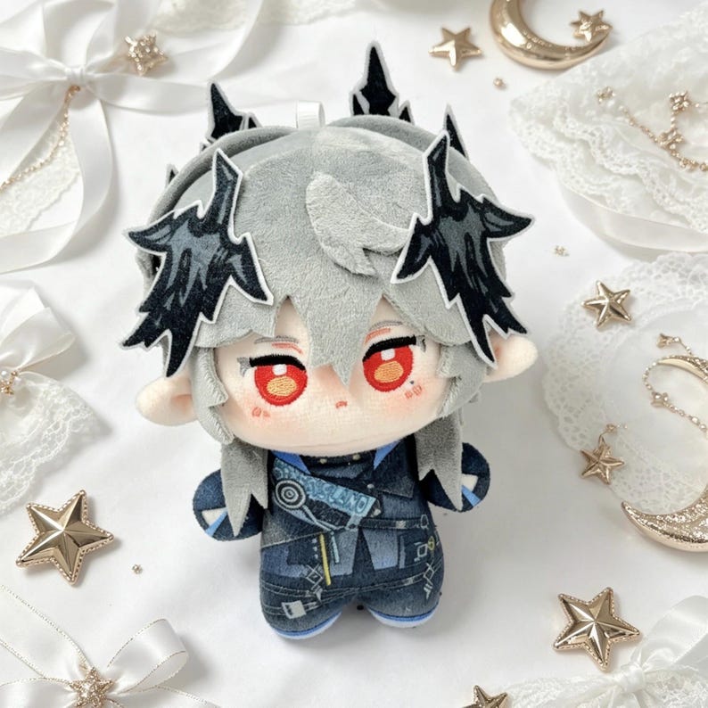May include: A plush doll with gray hair and black accents, red eyes, and a blue outfit. The doll has a detailed design, with a crown-like feature on its head. The background includes decorative stars and ribbons.