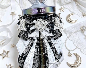 May include: A SEVENTEEN lightstick adorned with a decorative black and white ribbon bow featuring celestial patterns, silver butterfly charms, a central oval rhinestone brooch, and delicate silver chains draped across the layered fabric ribbons.