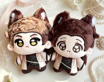 May include: Two plush dolls featuring animal ears, one with light brown fur and yellow eyes, the other with dark brown fur and brown eyes. Both dolls wear cream and dark brown outfits with intricate patterns, small arms, and embroidered facial features.