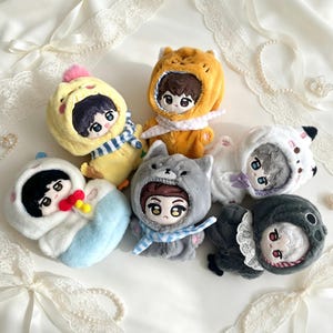May include: Six plush dolls with embroidered facial features, each wearing a different animal-themed hooded onesie. The dolls feature outfits including a yellow chick, an orange bear, a gray wolf, a white cat, a blue-and-white creature, and a dark gray animal.