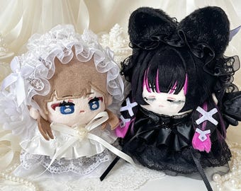 May include: Two plush dolls side by side. The left doll has light brown hair, blue eyes, and wears a white ruffled bonnet and dress with a pearl accent. The right doll has black hair with pink streaks, cat ears, and a black ruffled dress.