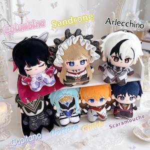 May include: A collection of six plush dolls arranged on a white shelf. The dolls are labeled with text: Columbina, Sandrone, Arlecchino, Capitano, Dottore, Childe, and Scaramouche. Each plush features distinct hair colors, outfits, and facial expressions.