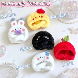 Puede incluir: Una colecci&oacute;n de cinco gorros de peluche para mu&ntilde;ecos con varios dise&ntilde;os: un conejo blanco con lazo morado, un pollito amarillo con boina roja, una criatura negra con mejillas rosas, un gorro blanco con un icono de helado azul y uno rojo.