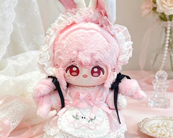 May include: A plush doll with pink hair and white rabbit ears, wearing a pink ruffled bonnet, clear glasses, and a pink dress with a white apron featuring an embroidered rabbit. The doll has large red eyes and black ribbons on its shoulders.