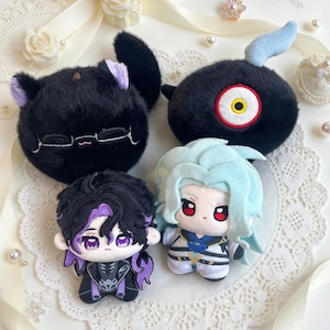 May include: A collection of four plush toys including a round black cat with purple ears, a black creature with a single yellow eye and blue horn, and two small human-like dolls with purple and light blue hair, all featuring detailed embroidery.