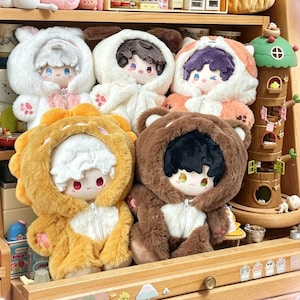 May include: A collection of five plush dolls wearing fuzzy animal-themed hooded onesies with zippers. The dolls feature soft, textured fabric in white, orange, yellow, and brown, with embroidered facial details and paw prints on the sleeves.