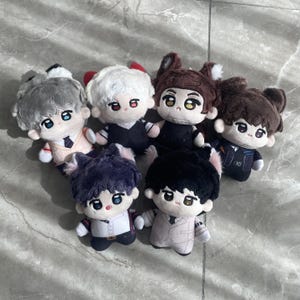 May include: A collection of six plush dolls featuring embroidered facial features, large eyes, and various hair colors including gray, white, brown, dark purple, and black. Each doll wears a distinct outfit, such as vests, shirts, and ties.
