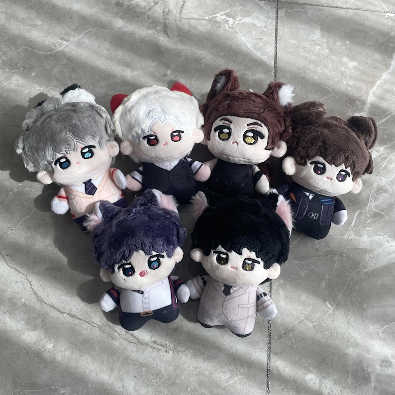 May include: A collection of six plush dolls featuring embroidered facial features, large eyes, and various hair colors including gray, white, brown, dark purple, and black. Each doll wears a distinct outfit, such as vests, shirts, and ties.