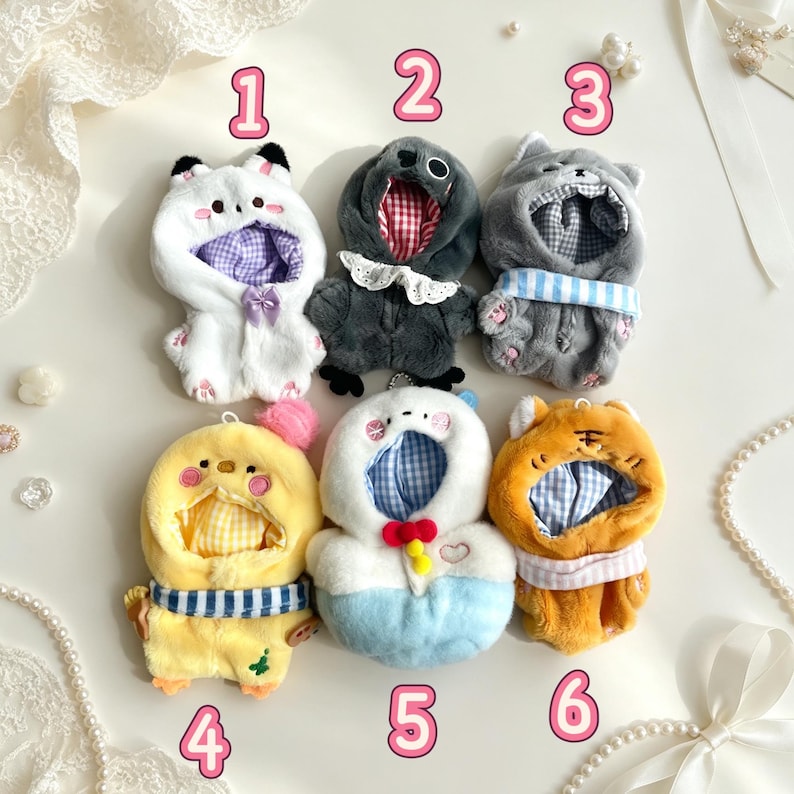 May include: Six plush animal-themed doll outfits with hoods, numbered 1 through 6. The collection includes a white cat, a dark gray bird, a light gray cat, a yellow chick, a white and blue character, and an orange tiger, all with fabric linings.
