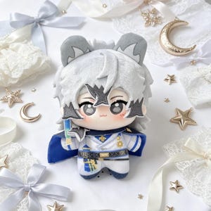May include: A plush doll with a white and gray wolf-like design, wearing a white uniform with blue accents. The doll has large eyes and is surrounded by decorative stars, bows, and lace.