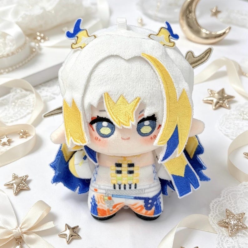 May include: A plush doll with white hair and yellow and blue accents. The doll has large blue eyes and is wearing a white and blue outfit. The doll is a cute, anime-style character.