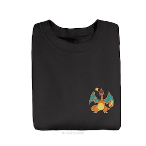May include: A black crewneck sweatshirt featuring a small embroidered graphic on the lower right side. The graphic depicts a cartoon orange dragon with blue wings, breathing fire from its mouth and holding a small flame in its left hand.