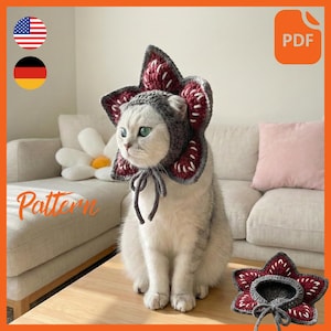 May include: A gray and burgundy crochet cat hat, resembling a Demogorgon from Stranger Things, worn by a white cat with green eyes. The hat is tied with a gray string. The word "Pattern" is written in orange script. A PDF icon is in the top right corner.