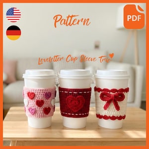 May include: Three white paper coffee cups with crocheted cup sleeves. The sleeves are pink with hearts, red with a heart, and cream with a bow. The image includes the text "Pattern" and "Loveletter Cup Sleeve Trio".