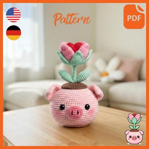 May include: A crocheted pink pig planter with a flower. The flower has pink and red petals and green leaves. The word "Pattern" is written in orange. The planter has black eyes and a brown top.