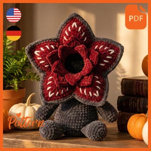 Könnte beinhalten: Eine handgefertigte Demogorgon-Plüschpuppe mit einem roten, blütenförmigen Kopf, grauen Blütenblättern und weißen Nähten. Der Körper ist grau und die Puppe sitzt auf einer Holzoberfläche. Das Wort "Pattern" ist sichtbar.