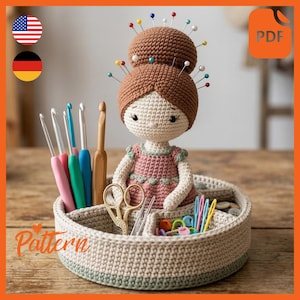 May include: A handmade crochet doll with a pin cushion head, holding crochet hooks, scissors, and other craft supplies in a round, divided basket. The doll wears a pink dress. The word "Pattern" is visible.