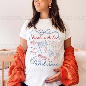 Op de afbeelding: Wit T-shirt met een rood en blauw patriottisch ontwerp, met de tekst "Red, white & Due" en illustraties van een Amerikaanse vlag, vuurwerk en andere symbolen van 4 juli. De persoon draagt een oranje trui.