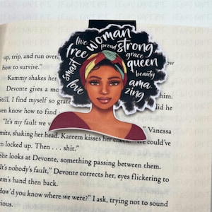 Puede incluir: Un marcap&aacute;ginas con una ilustraci&oacute;n de una mujer de piel oscura y cabello rizado. El dise&ntilde;o incluye las palabras "mujer", "fuerte", "reina" y otras palabras empoderadoras. El marcap&aacute;ginas est&aacute; colocado en las p&aacute;ginas de un libro.