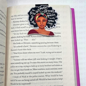 Puede incluir: Un marcap&aacute;ginas con la ilustraci&oacute;n de una mujer con un pa&ntilde;uelo en la cabeza y las palabras "woman, strong, queen, beauty, amazing". El marcap&aacute;ginas est&aacute; en un libro abierto.