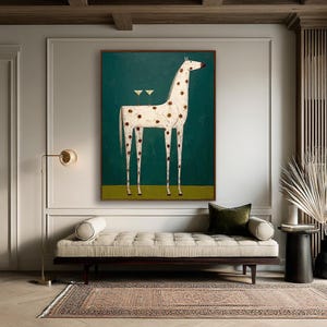 May include: A framed painting of a giraffe with brown spots and long legs, set against a teal background. Two martini glasses are depicted on the giraffe's back. The artwork is displayed above a beige chaise lounge.