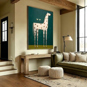 May include: A large framed painting depicts a giraffe with white fur and brown spots against a teal background. Two cocktail glasses are on the giraffe's back. The artwork hangs above a wooden console table in a living room setting.