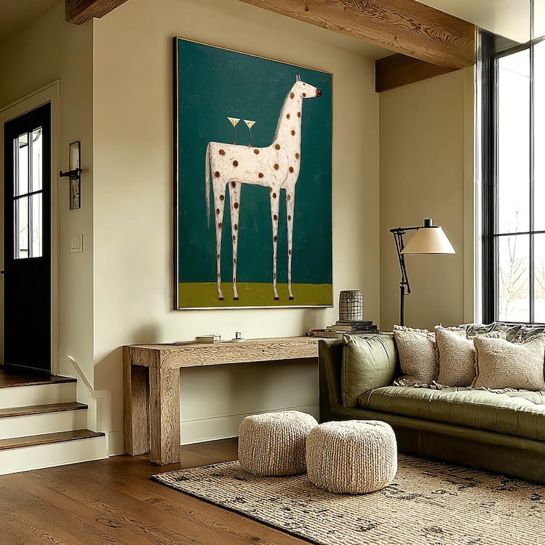 May include: A large framed painting depicts a giraffe with white fur and brown spots against a teal background. Two cocktail glasses are on the giraffe's back. The artwork hangs above a wooden console table in a living room setting.