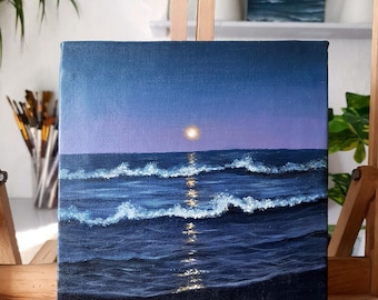 Puede incluir: Arte en lienzo cuadrado que representa una escena oceánica iluminada por la luna. La pintura presenta un mar azul oscuro con olas de cresta blanca que reflejan la luz de la luna. El cielo transiciona de azul oscuro a un tono púrpura más claro, con una luna brillante.