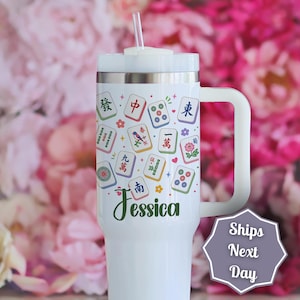 May include: A white stainless steel tumbler with a handle and a clear straw, featuring a colorful pattern of Mahjong tiles and small floral accents. The name Jessica is printed in dark green script near the bottom of the cup's main body.