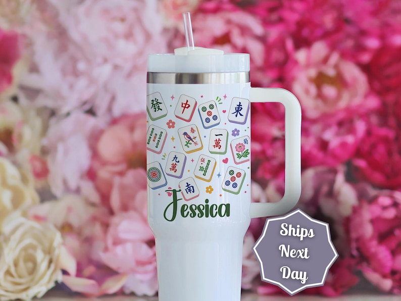 May include: A white stainless steel tumbler with a handle and a clear straw, featuring a colorful pattern of Mahjong tiles and small floral accents. The name Jessica is printed in dark green script near the bottom of the cup's main body.