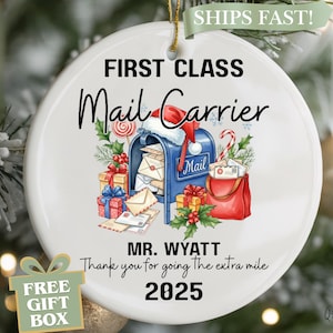 May include: White ceramic Christmas ornament with a festive design. It features a blue mailbox with a Santa hat, gifts, and the text "FIRST CLASS Mail Carrier". Includes the text "MR. WYATT" and "2025".