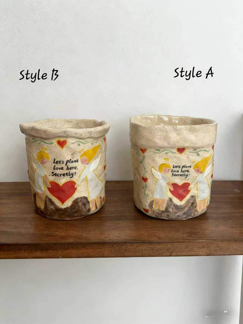 May include: Two ceramic planters, Style A and Style B, with a beige base and a textured rim. Each features a design of angels, a red heart, and the text "Let's plant love here. Secretly!" on the front. They sit on a wooden shelf.