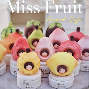 May include: A collection of whimsical ceramic fruit figurines, each with a small face peering out. The fruits include a yellow durian, a lemon, and strawberries, all resting on white pedestals. The text "Miss Fruit" and "Record Life" are visible.
