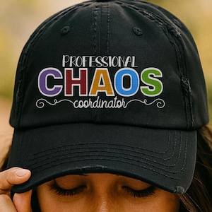 May include: Black baseball cap with the text "PROFESSIONAL CHAOS coordinator" in colorful letters. The hat has a distressed look and a curved brim. The text is in white, purple, red, orange, blue, and green.