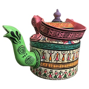 Puede incluir: Tetera decorativa pintada a mano con boquilla y asa verdes, con tapa con pomo morado. El cuerpo está adornado con patrones y figuras coloridas, incluyendo un borde rosa y una base blanca con figuras.