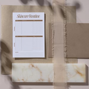 May include: A flat lay featuring a skincare routine checklist with the text "Skincare Routine" in brown. The checklist is on a white paper, with a brown background. Other elements include a marble tile, a brown envelope, and a beige ribbon.