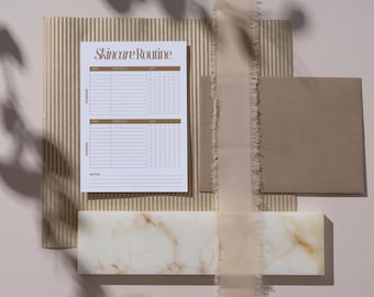 May include: A flat lay featuring a skincare routine checklist with the text "Skincare Routine" in brown. The checklist is on a white paper, with a brown background. Other elements include a marble tile, a brown envelope, and a beige ribbon.
