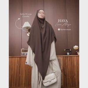 Puede incluir: Un cubrecabeza marrón oscuro y un vestido de color beige claro de manga larga. El texto en la imagen dice Sahla FK Long (Carafe), HAYA Linen Abaya y Buttercream. Un bolso de hombro acolchado blanco se lleva con el vestido de manga larga.