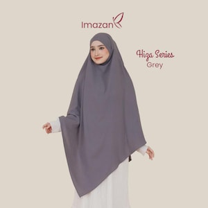 Può includere: Un hijab grigio a tinta unita della serie Imazan Hiza. Il copricapo presenta un tessuto liscio e drappeggiato che incornicia il viso e scende fino al busto. Il testo Imazan e Hiza Series Grey è stampato in rosso scuro sopra l'indumento.