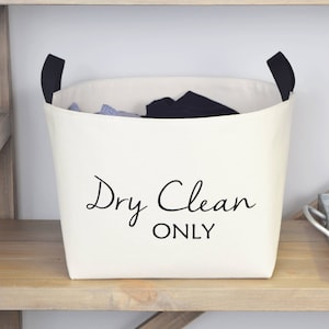 May include: White canvas laundry basket with black handles and the text "Dry Clean Only" printed on the front.
